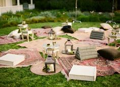 an outdoor seating area is set up on the grass with lanterns and rugs around it