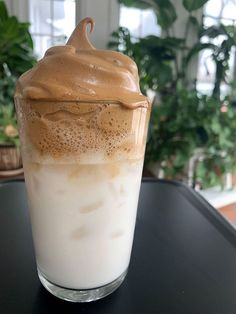 there is a drink with whipped cream in it on the table next to a potted plant