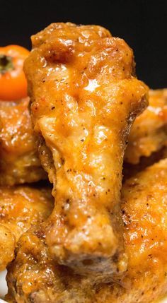 some chicken wings are sitting on a plate with a cherry tomato in the background,