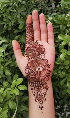 someone's hand with henna on it and green plants in the back ground