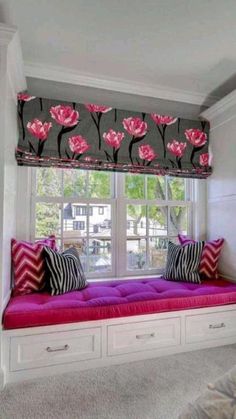 a window seat with pink flowers and black and white pillows on it in front of a large window