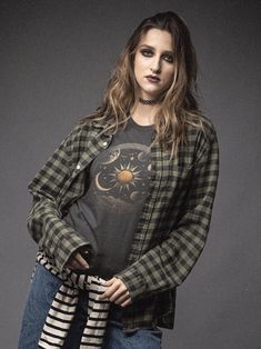 a woman with long hair wearing a black and white checkered shirt is standing in front of a gray background