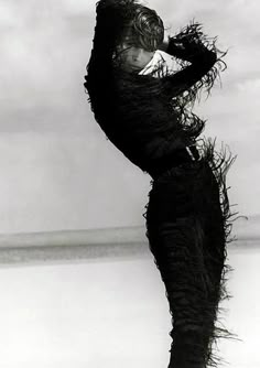 a black and white photo of a woman standing on the beach with her arms behind her head