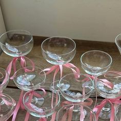 there are many wine glasses with pink ribbons around them on the wooden table and one is empty