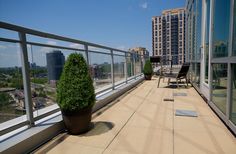 a balcony with chairs and potted plants on the floor next to glass windows overlooking cityscape