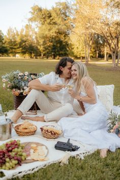 a man and woman sitting on top of a blanket next to each other holding wine glasses