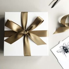 a white box with gold ribbon and a bee on it next to scissors, napkins and other items