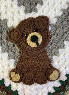 a crocheted brown teddy bear sitting on top of a white and gray blanket