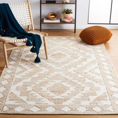 a white and beige area rug with an orange pillow on the floor next to it