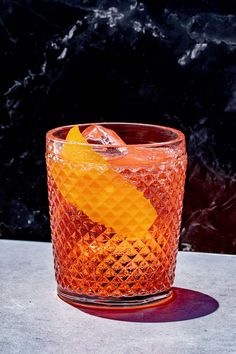 a glass with an orange slice in it on a table next to a marble wall