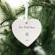 a white heart ornament hanging from a christmas tree with the words our first home written on it