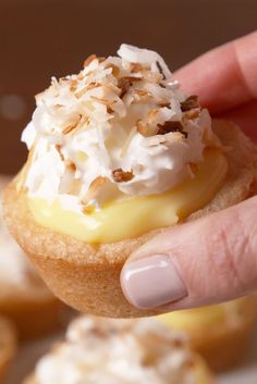 a hand holding a pastry with white frosting and toppings on it's top