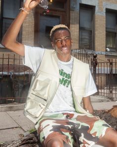 a man sitting on the ground with his hand up in the air and wearing camo shorts