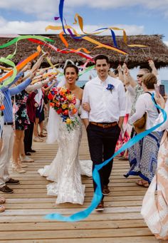 a bride and groom walking down a wooden walkway with streamers in the air as they exit their wedding ceremony