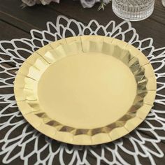 a white and gold plate sitting on top of a wooden table next to some flowers