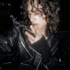 a woman with curly hair wearing a black leather jacket and holding her hand to her mouth