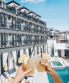 a person holding up a drink in front of a building with an outdoor swimming pool