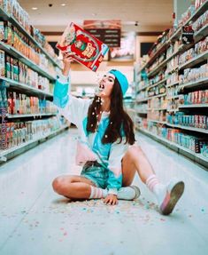 a woman sitting on the floor in a store aisle holding up a bag of cereal