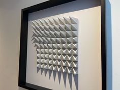 an abstract paper sculpture is displayed in a black frame on the wall next to a white wall