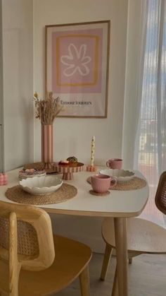 a dining room table with plates, cups and bowls on it in front of a window