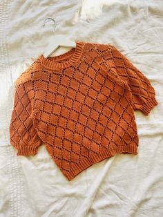 an orange sweater laying on top of a white bed next to a wooden hanger