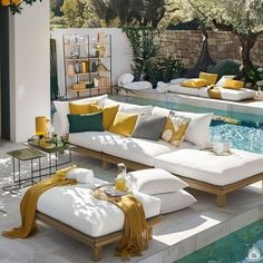 an outdoor living area with white couches and yellow throw pillows near a swimming pool