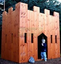 a young boy standing in the doorway of a wooden castle like structure that is made out of wood planks