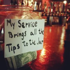 a jar filled with money sitting on top of a wooden table next to a bar