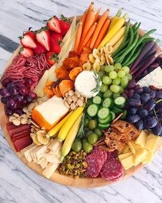 a platter filled with different types of cheeses, fruits and vegetables on a marble surface