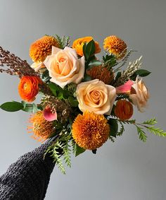 a vase filled with orange and white flowers on top of a table next to a gray wall