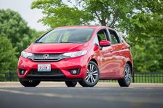 a red honda fit is parked on the side of the road in front of some trees