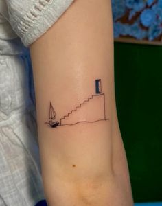 a woman's arm with a small tattoo of a boat on the water and stairs