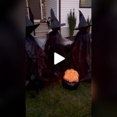 three witches standing in front of a house wearing black robes and holding an orange pumpkin