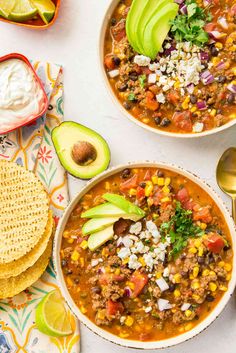 two bowls of chili and corn soup with tortilla chips, avocado