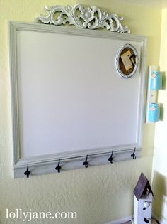 a white frame hanging on the wall with hooks and a birdhouse in front of it