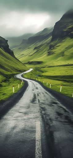 an empty road in the middle of a green valley with mountains behind it and cloudy skies overhead