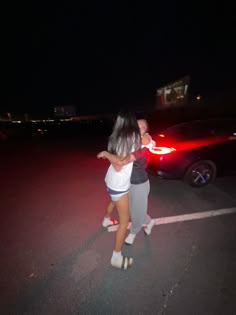 two people standing in the middle of a parking lot at night with their arms around each other