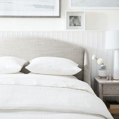 a bed with two white pillows on top of it next to pictures and a lamp