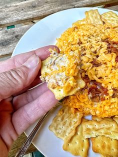 a person holding a fork over a white plate with crackers and cheese on it