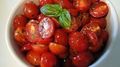 a white bowl filled with lots of fresh tomatoes and basil sprinkled on top