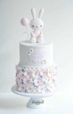 a white cake with pink and blue flowers on the bottom, topped with a bunny figurine