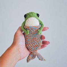 a hand holding a small knitted toy with a frog on it's back