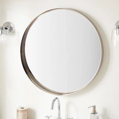 a bathroom sink with a round mirror above it and two faucets on the side