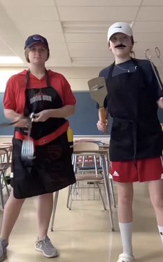 two girls in aprons are holding utensils and standing next to each other