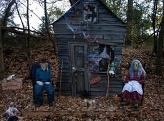 two people dressed up in halloween costumes sitting next to a small wooden house with ghost decorations on it