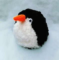 a black and white stuffed animal with an orange beak sitting in the middle of snow