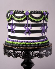 a black and white striped cake with purple flowers on it's top, sitting on a stand