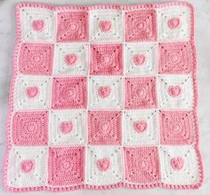 a pink and white crocheted afghan with hearts on the front, sitting on a marble surface