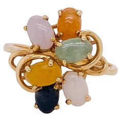 A depth of color and layers are the beauty of this ring. All of the jades in this ring are naturally occurring colors (white, black, yellow, lavender, orange, green). The everyday strength of jade often gives a source of strength for any who need it. A wire work frame is securely layered to hold each of the colorful jade cabochons along with swirling scroll work accents near the shoulders of the band. The ring top design forms a circle that measures 17.5 millimeters in diameter. This charmer was made in Hong Kong (stamped: 585 Hong Kong 14K) and is built to be slender yet strong. The full details for this beautiful ring are listed below: Metal Quality: 14 karat yellow gold Complete Ring Weight: 3.7 grams Ring Size: 8.25 (sizing not included) Band Width: Center design 17.5 mm in diameter, s Multicolor Cabochon Rings In Fine Jewelry Style, Multicolor Cabochon Rings Fine Jewelry, Fine Jewelry Multicolor Cabochon Gemstones, Multicolor Cabochon Gemstones For Fine Jewelry, Multicolor Cabochon Gemstones Fine Jewelry, Multicolor Oval Rings With Natural Stones, Vintage Cluster Ring, Lavender Orange, Scroll Work