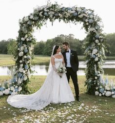 a bride and groom standing in front of an arch with flowers on the grass at their wedding